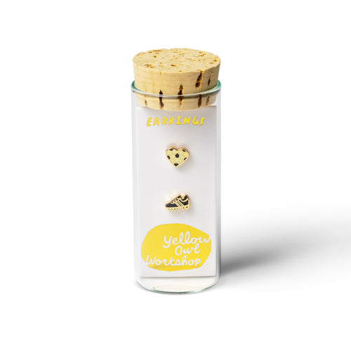 Yellow Owl Workshop Soccer Love mismatched stud earrings displayed in signature glass vial packaging with a cork stopper. Gold-tone enamel soccer ball heart and soccer cleat earrings, a fun soccer-themed jewelry gift for soccer players, coaches, and soccer fans.