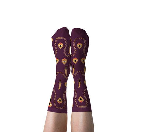 A pair of purple crew socks with a heart and dagger pattern, worn on a person's legs against a white background.