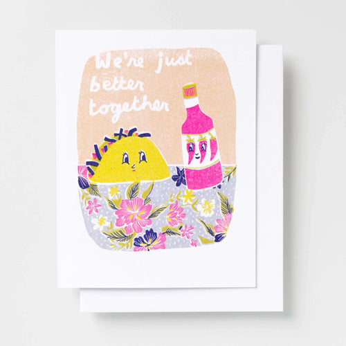 Risograph greeting card with illustrated taco and hot sauce bottle characters sitting together in a field of flowers on a peach background, text reads We're Just Better Together in white handwritten lettering