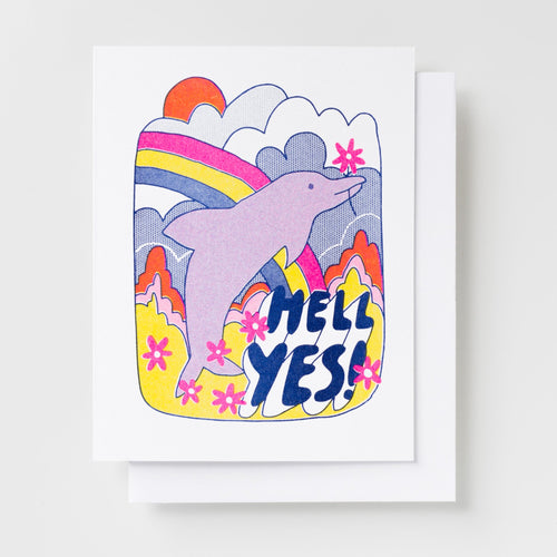 Risograph greeting card with an illustrated pink dolphin leaping through a colorful psychedelic landscape with a rainbow, clouds, and pink flowers, text reads Hell Yes in bold navy lettering