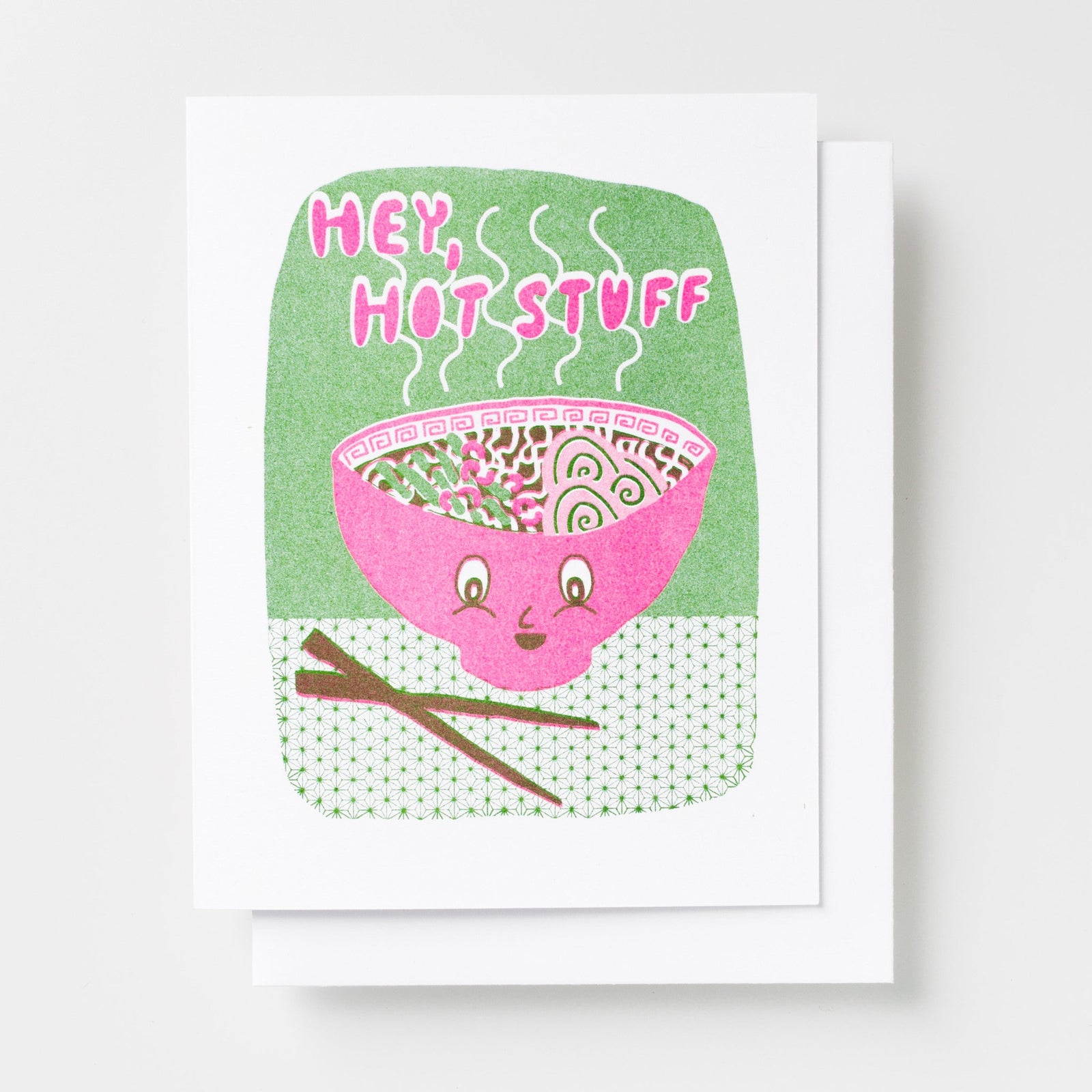 Risograph greeting card with an illustrated smiling pink ramen bowl with chopsticks and steam rising on a green background, text reads Hey Hot Stuff in bold pink lettering