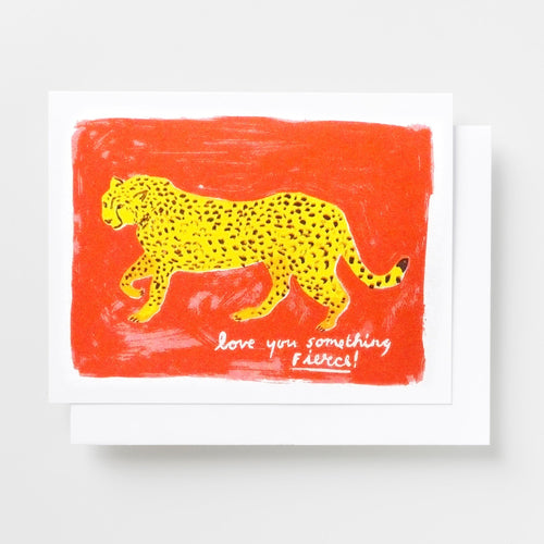 Risograph greeting card with an illustrated yellow leopard walking across a bold red background, text reads Love You Something Fierce in white handwritten lettering