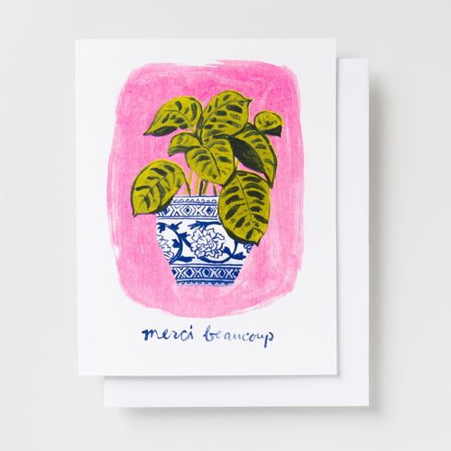 Risograph greeting card with an illustrated green leafy plant in a blue and white chinoiserie vase on a bold pink background, text reads merci beaucoup in navy handwritten lettering