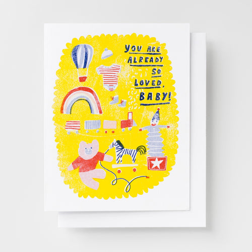 Risograph greeting card with illustrated baby toys including a teddy bear, zebra pull toy, hot air balloon, rainbow, clown, and onesie on a bright yellow scalloped background, text reads You Are Already So Loved Baby in navy lettering