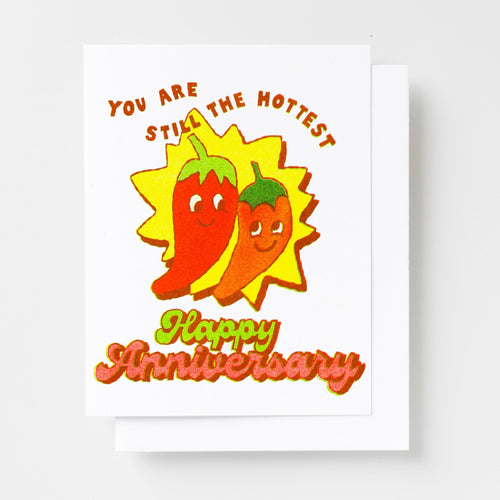 Risograph greeting card with two smiling chili pepper characters on a yellow starburst, text reads You Are Still the Hottest Happy Anniversary in red and green lettering
