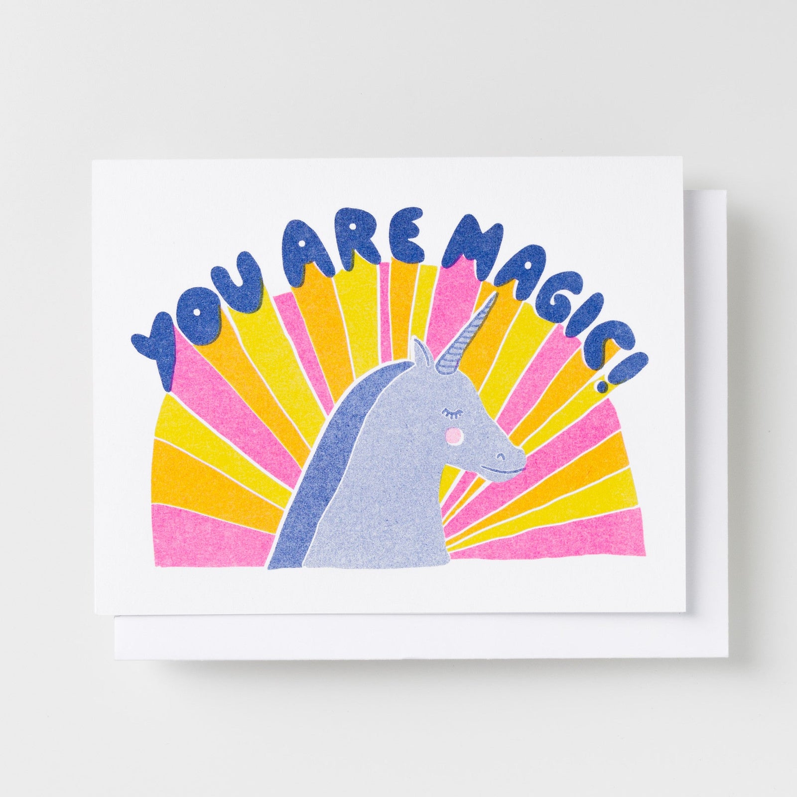 Risograph greeting card with an illustrated blue unicorn against a bold pink and yellow sunburst background, text reads You Are Magic in large blue bubble lettering