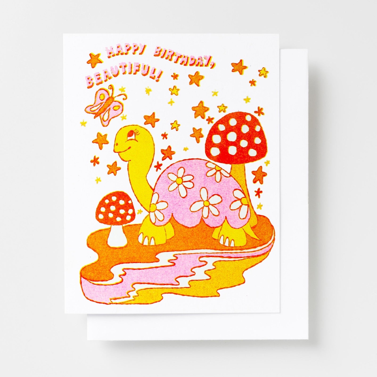Risograph greeting card with an illustrated turtle covered in daisy flowers surrounded by red mushrooms, stars, and a butterfly in orange, pink, and yellow tones, text reads Happy Birthday Beautiful in curved lettering