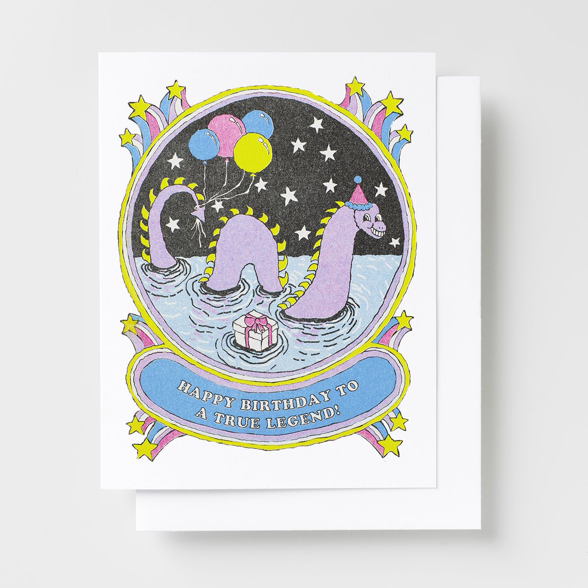 Risograph greeting card with an illustrated Loch Ness Monster wearing a party hat surrounded by balloons and stars on a dark night sky background, text reads Happy Birthday to a True Legend on a blue banner